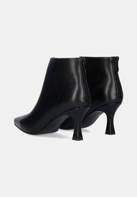 Botas de tobillo de cuero negro con punta afilada y tacón cónico. Presentan un detalle de cremallera en la parte trasera para el cierre y una textura suave.