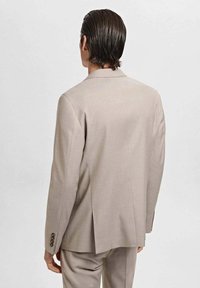 Beige tailored suit jacket with a straight cut, subtle texture, single vent at the back, and four-button detailing on the cuffs.