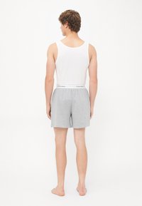 Weißes ärmelloses Tanktop und graue Shorts mit einem weißen Calvin Klein Bund, hergestellt aus weichem Stoff und im lässigen Schnitt. Keine sichtbaren Muster.