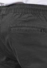 Mustat, joustavavyötäröiset housut, joissa on sileä pinta. Takana on päällystasku ja hillitty brändäystunniste. Moderni ja toiminnallinen muotoilu.