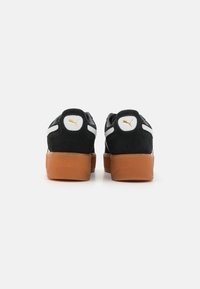 Adidași negri din suede cu o talpă din cauciuc de tip gumă, dungi albe pe laterale și accente aurii pe toc și limbă. Design cu vârf rotunjit.