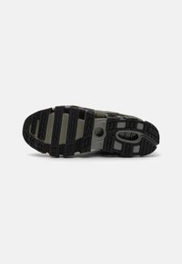 Black and gray athletic shoe sole with ridged texture, featuring circular cutouts and varying panel designs for enhanced grip and support.