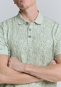 Lichtgroene polo met een gestructureerd patroon, knoopsluiting op de kraag en korte mouwen met contrasterende manchetten en afwerking.