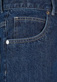 Gros plan d’un jean en denim bleu foncé montrant la poche avant, la petite poche et les détails de couture avec un rivet en métal.