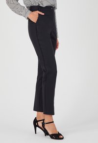 Pantaloni neri aderenti con vita alta, tasche laterali e dettagli di cucitura a contrasto. Abbinati a sandali neri con tacco.
