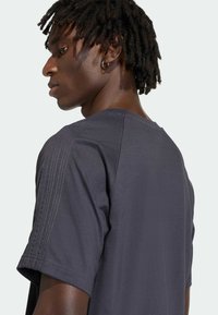 Tmavosivá tričko s krátkym rukávom a okrúhlym výstrihom, s vertikálnymi švami na ramenách a hladkou textúrou.