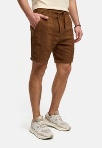 Brune teksturerede shorts med en snoretræk i livet, sidelommer og rullede kanter, parret med lyse beige sportssko.