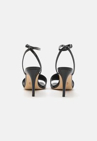 Black heeled sandals featuring an open back, crossed ankle straps, and a sleek design. The heel is slender and high, with a smooth finish.
