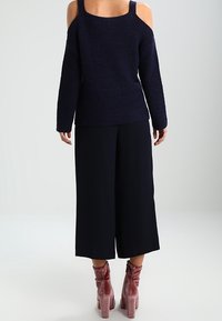 Marinblå stickad tröja med kallaxel-design, kombinerad med vida svarta byxor. Outfiten inkluderar rosa sammetstövletter.