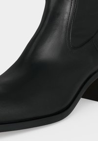 Bottine en cuir noir avec talon bloc et panneau latéral élastique, présentée sur un fond clair.