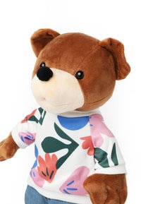 Ours en peluche marron avec un museau beige clair, portant un sweat-shirt coloré à motif floral et un jean bleu. Texture douce et forme arrondie.