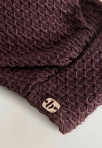 Dziergany ciemnofioletowy szalik z teksturowanym wzorem diamentowym i złotymi nitkami, z metalową metką marki jako akcentem.