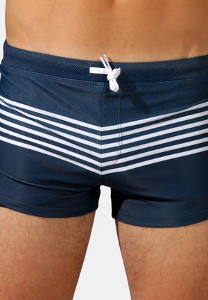 Shorts de bain navy avec un motif en chevrons, comportant des rayures blanches horizontales et un cordon blanc pour un ajustement réglable.