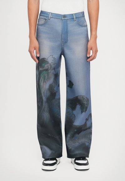Jeans de pierna ancha en denim azul claro con un patrón abstracto oscuro. Incluye cinco bolsillos, cierre de botón y un ligero desgaste.