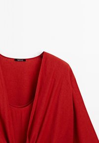 Červený lněný zavinovací top s hlubokým výstřihem do V, drapovaným designem a krátkými rukávy, s hladkou texturou a malou kapsou.