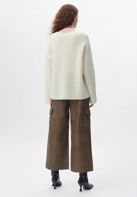 Übergroßer cremefarbener Strickpullover mit geripptem Muster, kombiniert mit dunkelbraunen Cargo-Hosen mit Taschen und weißer Naht. Schwarze Stiefel mit Absatz.