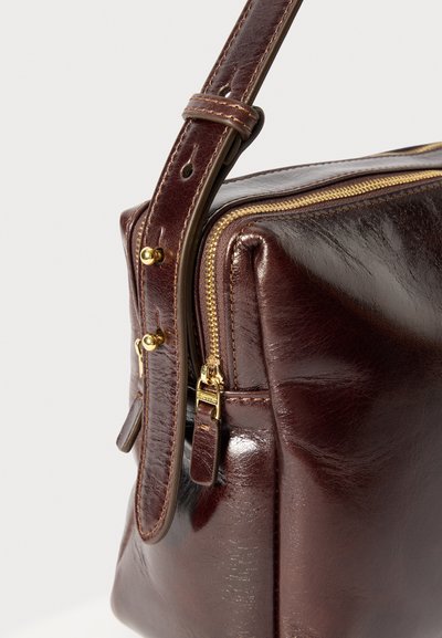 Brown leather handbag with a shiny finish, gold zipper closure, adjustable strap, and detailed stitching. Features a rectangular shape.