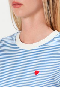 Blå och vit randig t-shirt med rund halsringning och vit ribbad kant, med ett litet rödbroderat hjärta på bröstet.