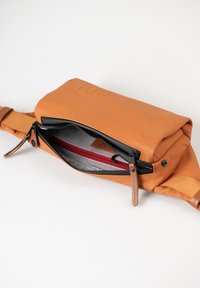 Orange Ledertasche mit grauem Innenfutter, ausgestattet mit einem Reißverschlussfach und roten Akzenten. Verstellbarer Riemen und Logo-Prägung auf der Vorderseite.