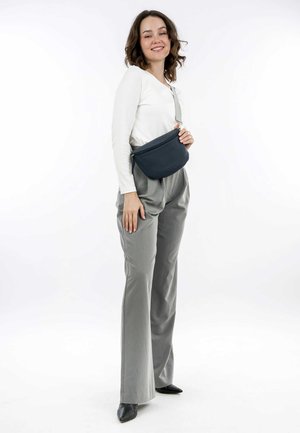 Gray fabric fanny pack with a curved design, zip closure, and adjustable strap worn over a white long-sleeve shirt and gray trousers.