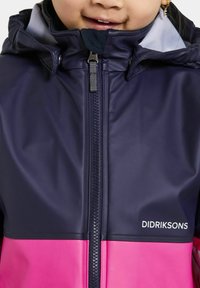 Navy en roze waterdichte jas met een hoge kraag, volledige rits en capuchon. Bevat een zachte binnenvoering en het merklogo aan de onderkant van de voorkant.