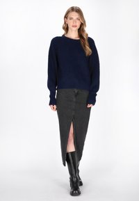Marineblauer Strickpullover mit lockerer Passform, kombiniert mit einem hochgeschnittenen schwarzen Denimrock mit einem Schlitz vorne. Schwarze kniehohe Stiefel.