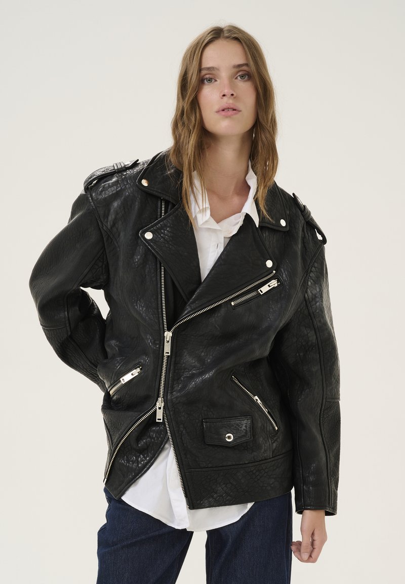 Giacca da biker in pelle nera con zip asimmetriche, texture a rilievo, spalline e dettagli in metallo argentato.