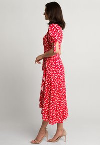 Czerwona sukienka w kwiaty z bufiastymi rękawami, bocznymi wiązaniami i warstwowym dołem. Wykonana z lekkiego materiału w intensywny wzór małych białych kwiatków.