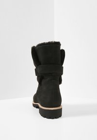 Svart ankelboot med en mocka-finish, mjukt pälsklädd foder, justerbar rem och en texturerad gummisula. Har en rund tå och stickade detaljer.