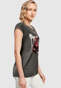 Kulfarvet kortærmet t-shirt med grafisk tryk, der viser en rød karakter og tekst, rund halsudskæring og en afslappet pasform.