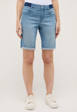 Un mannequin porte un short en jean bleu clair aux ourlets retroussés, un haut blanc et des baskets blanches sur un fond uni.