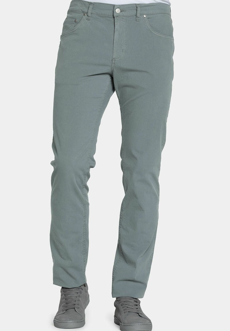 Muž v světlých šedých slim-fit kalhotách a ladících šedých šněrovacích teniskách, stojící na jednobarevném pozadí.