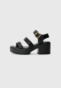 Sandalias de tacón de cuero negro con tres tiras anchas, cierre de hebilla lateral y suela gruesa con tracción texturizada.