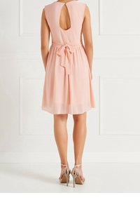 Růžové bezramenní šaty s výřezem na zádech, s úzkým pasem a mašlí. Materiál je hladký a lehký, v kombinaci s sandály na pásky.