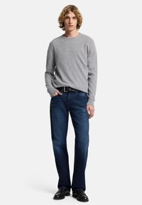 Maglione grigio a collo rotondo con maniche lunghe, abbinato a jeans blu scuro e scarpe nere. L'outfit presenta una vestibilità rilassata e un design classico.