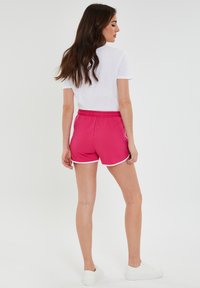 Roze shorts gemaakt van zachte stof met een witte trim. Voorzien van een elastische tailleband en een relaxte pasvorm, gecombineerd met een eenvoudig wit T-shirt.
