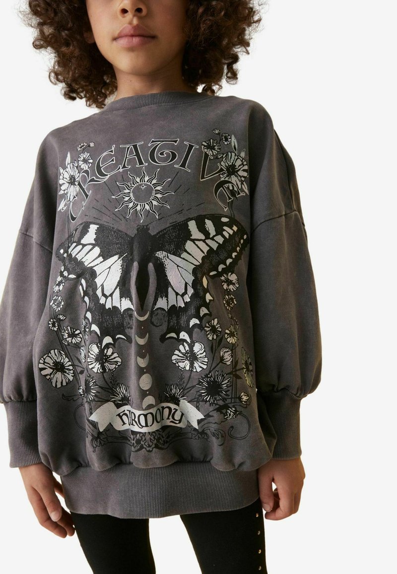 Grå oversize sweatshirt med en fjärils grafik, blommönster och texten "Kreativ Harmoni." Ribbad mudd och nederkant.