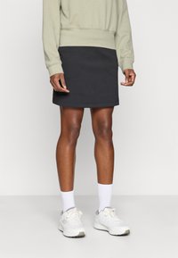 Svart skjørt med en tettsittende design, med to lommer foran. Kombinert med en lys grønn sweatshirts og hvite treningessko med grå detaljer.