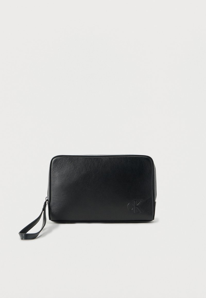 Μαύρο τσαντάκι από δέρμα με απαλή υφή, ορθογώνιο σχήμα, κλείσιμο με φερμουάρ και λουράκι για τον καρπό. Διαθέτει ανάγλυφο λογότυπο στο μπροστινό μέρος.