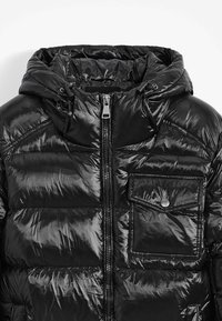 Veste doudoune noire rembourrée avec une surface brillante et matelassée. Elle dispose d'une fermeture éclair, d'une capuche ajustable et d'une poche à pression à l'avant.