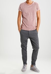 Ljust rosa, kortärmad t-shirt med textilstrukturer som kombineras med mörkgrå, avsmalnande bomullbyxor. Grå sneakers fulländar outfiten.