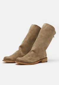 Botas altas de ante marrón, con punta redondeada, acabado texturizado y un bajo tacón de madera. Presentan un pequeño zipper en la parte trasera.