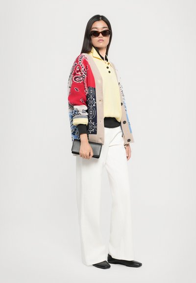 Cardigan en tricot avec des motifs paisley multicolores, top jaune, pantalon large blanc, chaussures noires et une pochette noire.