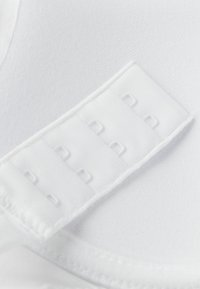 Vit plagg med en slät, texturerad tyg. Funktionen inkluderar en krok-och-öga-stängning med fem vita öglor och rektangulära öppningar.