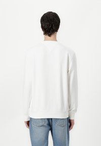 White sweatshirt with a crew neck and ribbed cuffs, featuring a smooth texture and a relaxed fit, paired with light blue jeans.