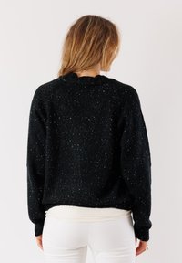 Maglione nero lavorato a maglia con vestibilità rilassata, caratterizzato da un motivo testurizzato e punte di filo chiaro. Il bordo e i polsini a coste contrastano con il design.