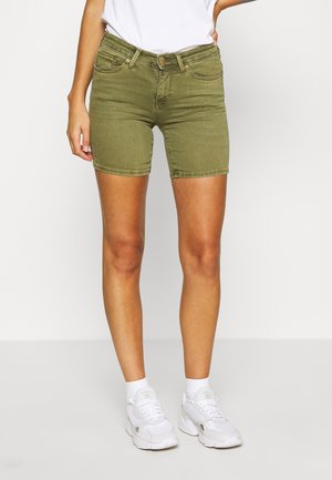 Shorts en denim vert olive au design ajusté, avec des poches avant et des détails de couture, associés à des baskets de sport blanches.