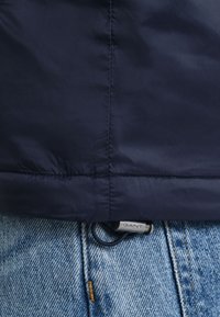 Mornarska podstavljena jakna s glatkom teksturom i zatvaračem. Sadrži suptilan logotip i kontrastne šavove na svijetloplavom denimu.