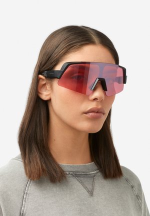 Ochelari de soare supradimensionați negri cu un design unghiular ascuțit și lentile cu gradient roșu, având o ramă robustă și o punte a nasului distinctivă.