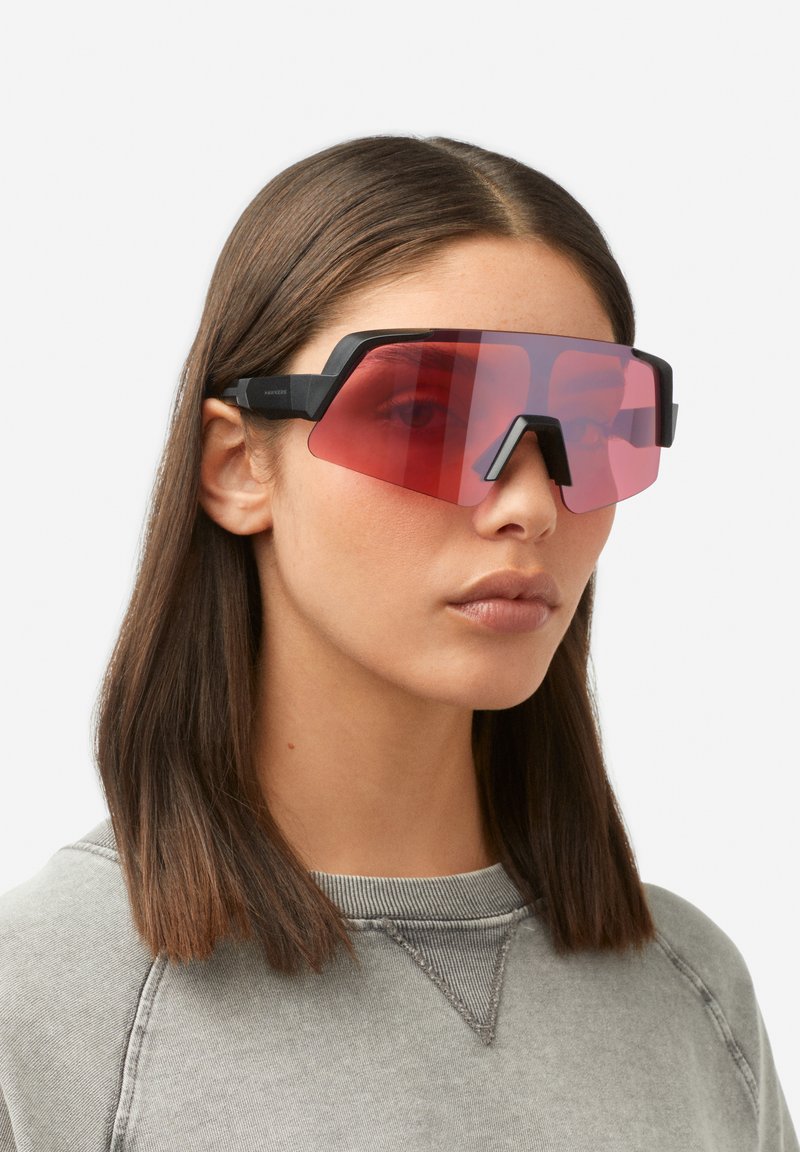Črna prevelika sončna očala z ostrim kotnim dizajnom in rdečim gradientnim lečam, s trdnim okvirjem in značilnim nosnim mostom.